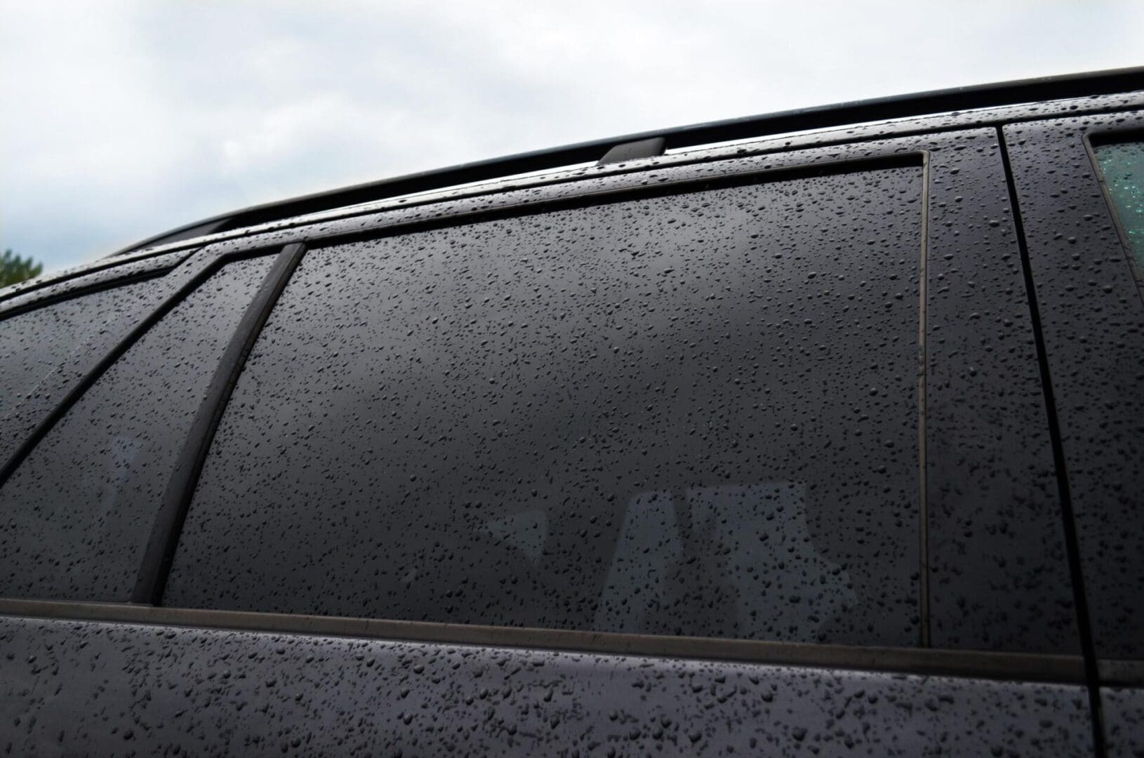 A close-up of a car window with raindrops covering its surface.